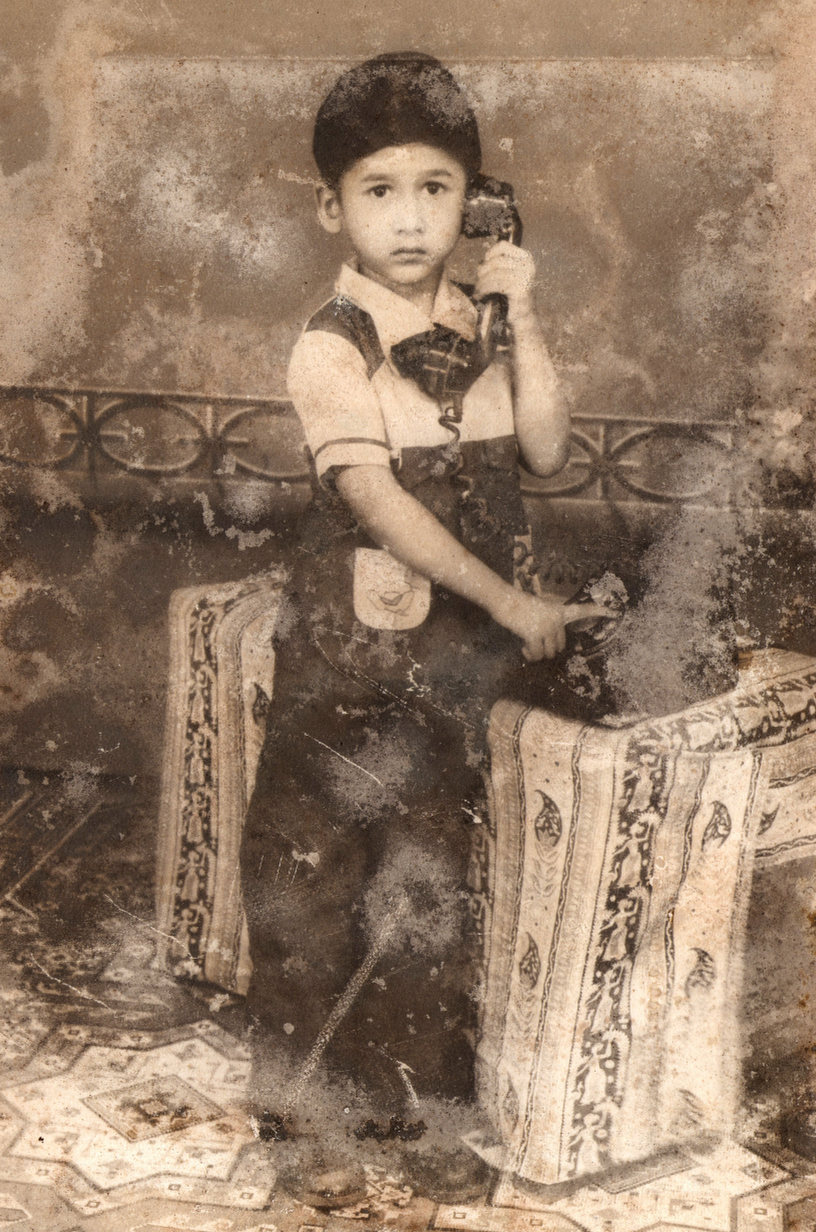 A mould-damaged photograph of a boy on the telephone, before restoration